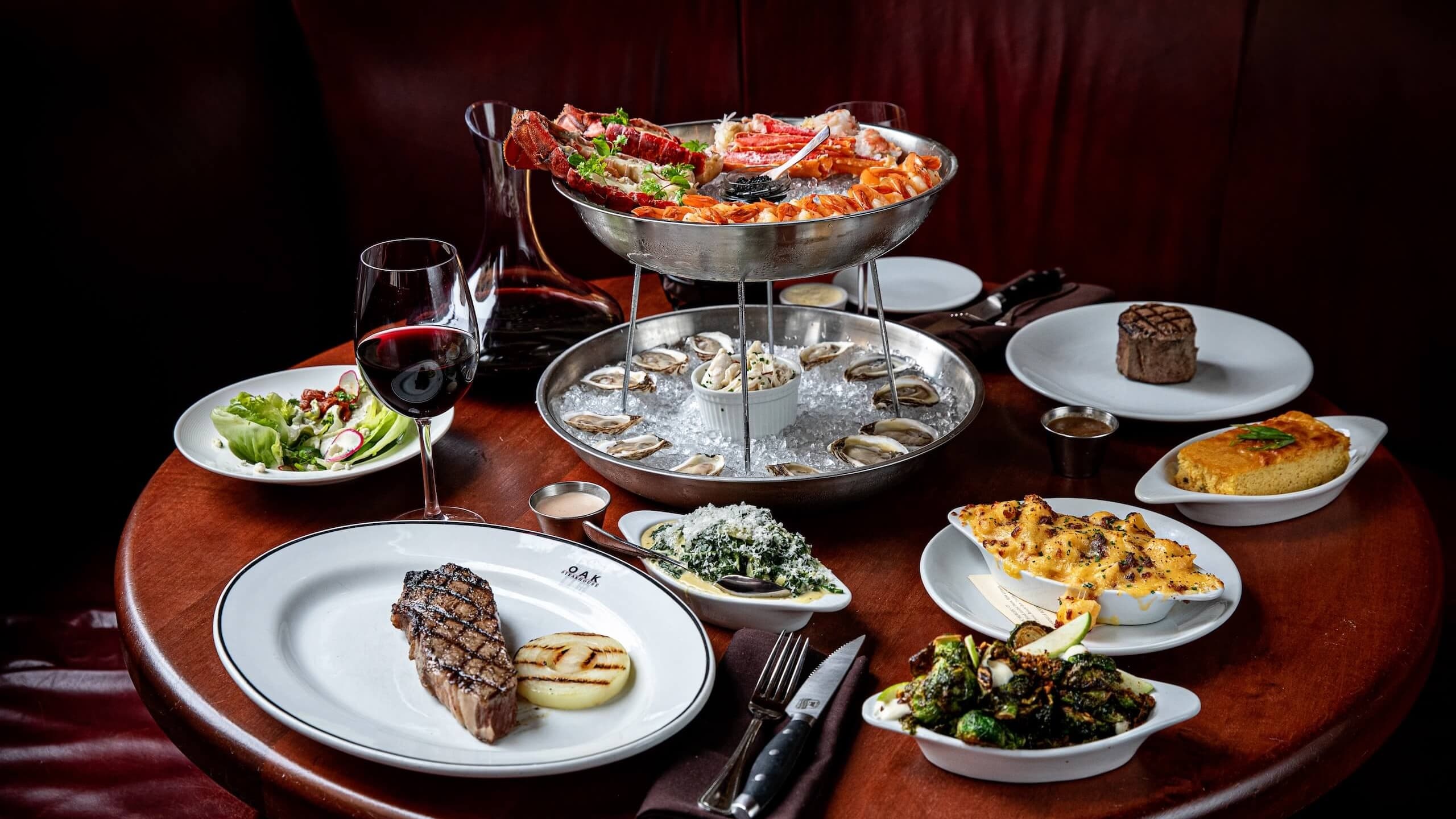 Fine dining spread featuring grilled steaks, fresh oysters, lobster, and gourmet sides at Oak Steakhouse in Savannah's Historic District, Georgia.
