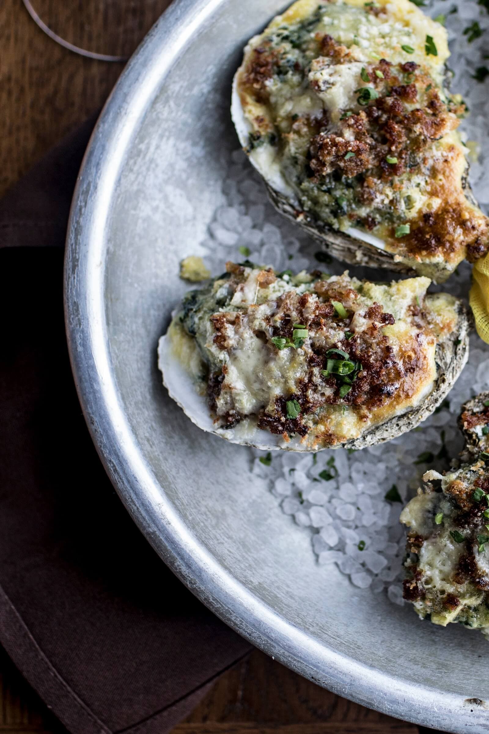 Baked oysters topped with herbs and golden cheese on a bed of ice, showcasing the upscale seafood dining experience at Oak Steakhouse in Savannah, Georgia.