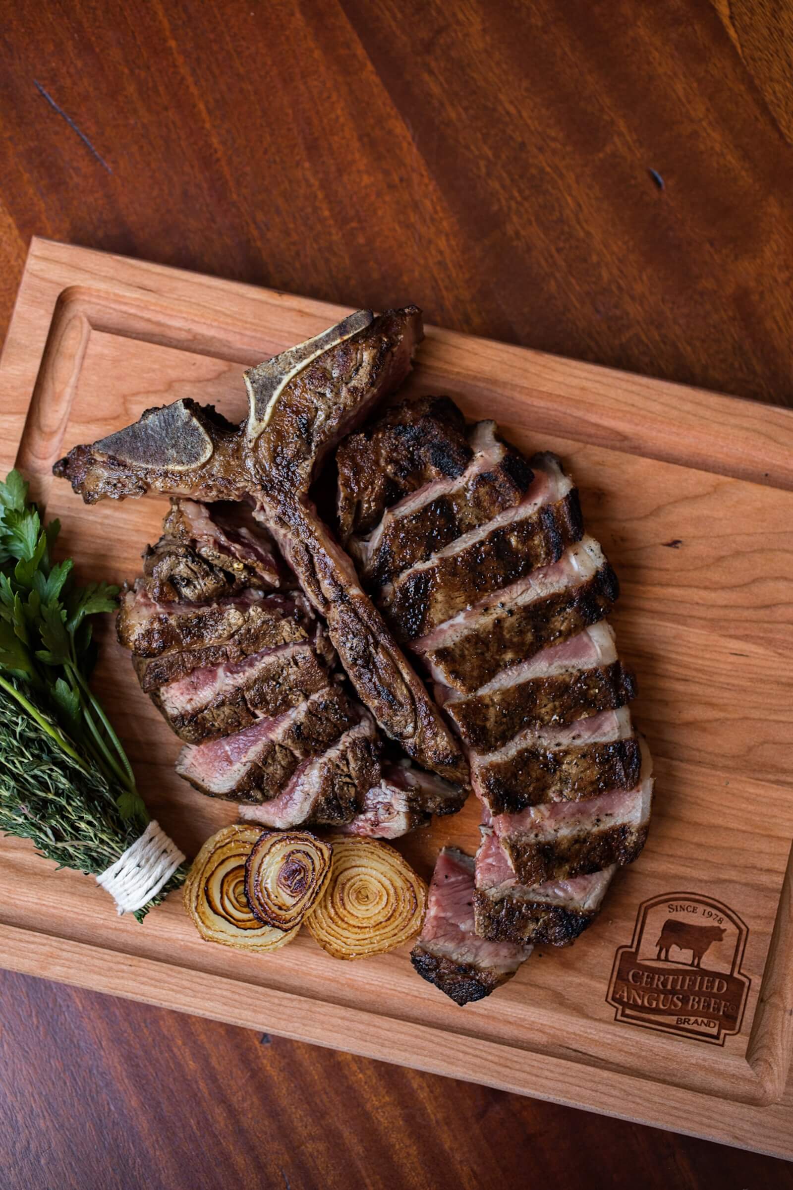 Sliced grilled steak served on a wooden board with fresh herbs at Oak Steakhouse, a fine dining restaurant in Savannah's Historic District.