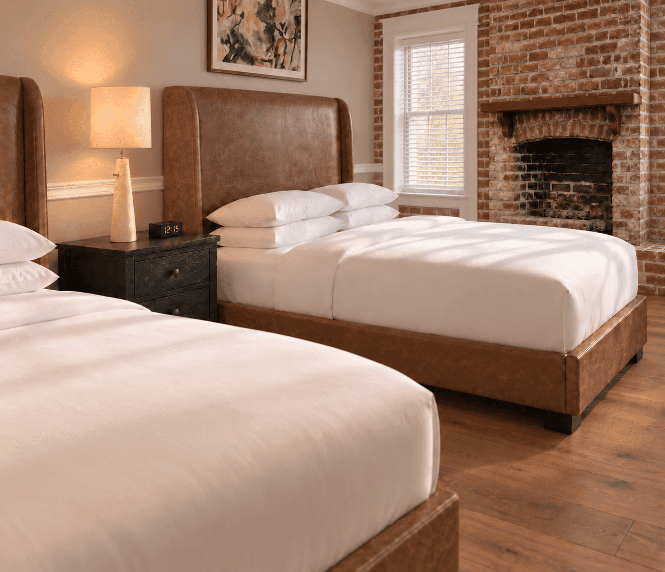 Heritage Double Queen room at Sabal House Inn in Savannah's Historic District, featuring two queen beds, hardwood floors, and an original exposed brick fireplace.